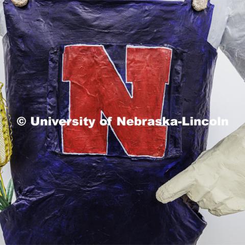 Ears of corn stick out of the pocket of the papier mâché Herbie. Dohe, Administrative Coordinator for Electrical and Computer Engineering, has made an 8-foot tall Herbie Husker from paper- mâché. She hopes to auction it off to help veterans. October 30, 2023. Photo by Craig Chandler / University Communication.