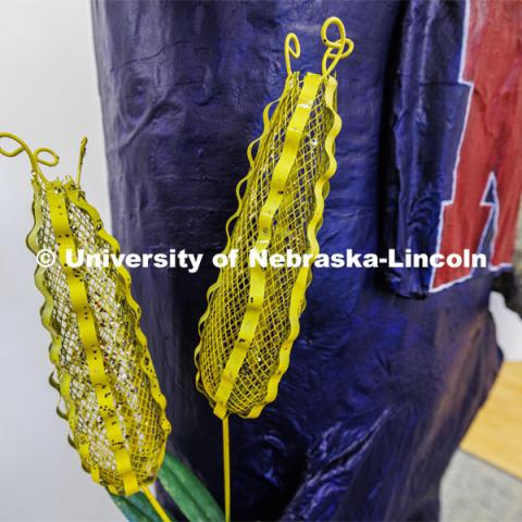 Ears of corn stick out of the pocket of the papier mâché Herbie. Dohe, Administrative Coordinator for Electrical and Computer Engineering, has made an 8-foot tall Herbie Husker from paper- mâché. She hopes to auction it off to help veterans. October 30, 2023. Photo by Craig Chandler / University Communication.