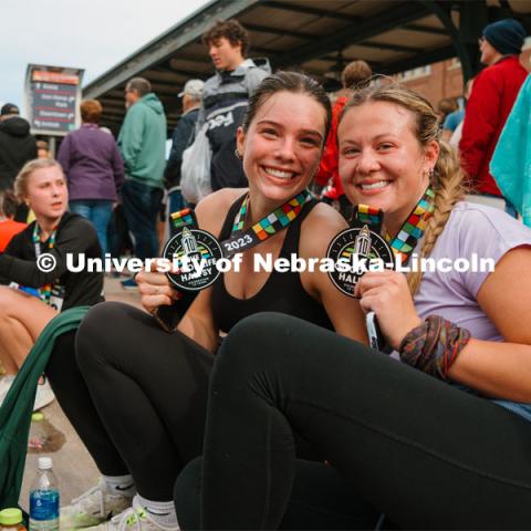 Runners show off their medals. The Good Life Halfsy half marathon runs through the streets of Lincoln and end downtown in the Haymarket. About Lincoln at the Good Life Halfsy. November 5, 2023. Photo by Matthew Strasburger / University Communication.