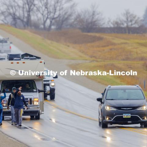 Iowa veterans Dawn Walton and Casey Swanson wave to a passing car as they walk with their group along Hwy 83 east of Atlantic, Iowa, carrying the Nebraska v. Iowa game ball. The Things They Carry" ruck march involving military and veteran students from Iowa and Nebraska. To raise awareness about veteran suicide, through the week, the students walk in 20-mile shifts carrying 20-pound backpacks to commemorate the estimated 20 veterans who die by suicide each day. November 20, 2023. Photo by Craig Chandler / University Communication and Marketing.