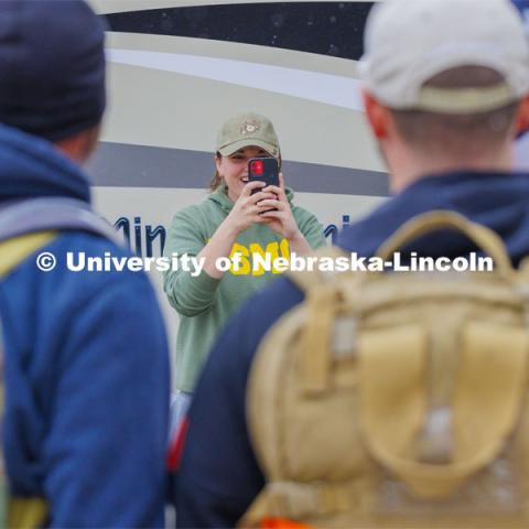 Jenalee Wimer, a senior Animal Science Pre-Veterinary Medicine student and a Marine, takes a photo of the Monday afternoon marchers. Ruck Marchers walk along Hwy 83 east of Atlantic, Iowa, carrying the Nebraska v. Iowa game ball. The Things They Carry" ruck march involving military and veteran students from Iowa and Nebraska. To raise awareness about veteran suicide, through the week, the students walk in 20-mile shifts carrying 20-pound backpacks to commemorate the estimated 20 veterans who die by suicide each day. November 20, 2023. Photo by Craig Chandler / University Communication and Marketing.