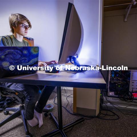 Luke Farritor works to decipher more of the scroll texts from his computers in his Kauffman Residence Hall room. He has set up a workstation on a table inside the door to the suite with his computer stored in a closet. Farritor, a senior in the Jeffrey S. Raikes School of Computer Science and Engineering, recently won a global contest to read the first text inside a carbonized scroll from the ancient Roman city of Herculaneum. That text had been unreadable since the eruption of Mount Vesuvius in A.D. 79. Farritor developed a machine-learning algorithm that detected the Greek word πορϕυρας (purple) on the charred papyrus scroll, which is too delicate to unroll using MRI scans. November 27, 2023. Photo by Craig Chandler / University Communication and Marketing.