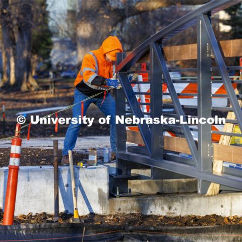 Lukas Lorenz with Judds Brothers Construction aligns the bridge as it is lowered onto the bolts on the west side of the creek. A new footbridge over Dead Mans Run on East Campus’ Maxwell Arboretum. December 5, 2023. Photo by Craig Chandler / University Communication and Marketing.
