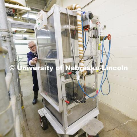 Paul Kononoff wheels a methane-measuring booth through the cattle barn. Kononoff, Professor of Animal Science, is measuring methane gas produced by cattle. To measure the gas, a cow is surrounded by a phone-booth like structure where the cow eats and drinks as the air is collected and sampled. December 15, 2023. Photo by Craig Chandler / University Communication and Marketing.