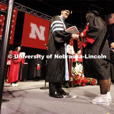 Crandall Blake receives her CEHS diploma from acting dean Nicholas J. Pace. Blake is wearing high top tennis shoes she had her kindergarten students she student taught sign so they could walk on stage with her. Winter undergraduate commencement in Pinnacle Bank Arena. December 16, 2023. Photo by Craig Chandler / University Communication and Marketing.