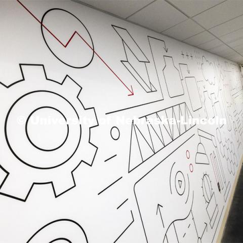 Workers apply graphics in the basement hallway connecting Kiewit and Othmer halls. January 16, 2024. Photo by Craig Chandler / University Communication and Marketing.