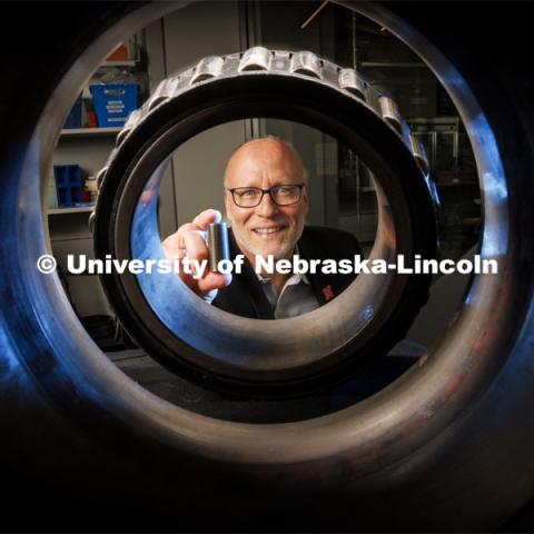 Joe Turner, Professor of Mechanical Engineering, holds a 3-D printed railcar bearing. He is photographed through an actual bearing and housing that fits on the end of each axle of a railcar axle. March 27, 2024. Photo by Craig Chandler / University Communication and Marketing.
