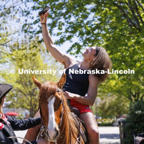 Josiah Allick takes a selfie as he rides Popsicle being led by Rodeo Club member Jaya Nelson. The Nebraska Rodeo Team gave Huskers a chance to be up close to their horses and even go for a ride. The team filled the space northwest of the Union to help promote their Nebraska Cornhusker College Rodeo being held Friday and Saturday. April 29, 2024. Photo by Craig Chandler / University Communication and Marketing.