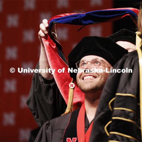 Zachery Shomo watches as his doctoral hood is lowered over his head. Graduate Commencement. May 17, 2024. Photo by Craig Chandler / University Communication and Marketing.