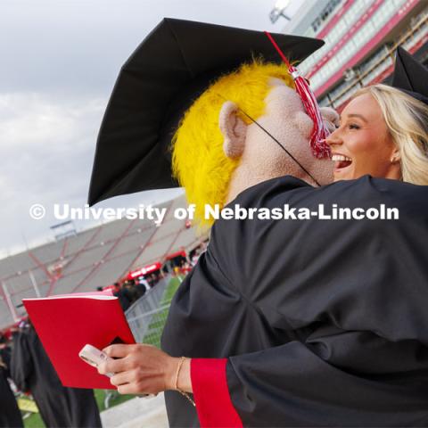 Skylar Hoxie hugs Herbie Husker as she enters the Memorial Stadium field for commencement. Undergraduate Commencement in Memorial Stadium. May 18, 2024. Photo by Craig Chandler / University Communication and Marketing.