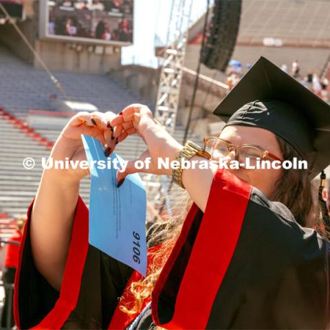 Maggie Nielsen, a Global Studies and Advertising Public Relations double major, holds up a heart to friends in the crowd. Undergraduate Commencement in Memorial Stadium. May 18, 2024. Photo by Kristen Labadie / University Communication.