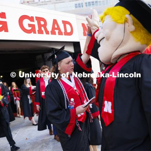 Caleb Pruss-Hansen high-fives Herbie Husker as the graduates enter the field. Undergraduate Commencement in Memorial Stadium. May 18, 2024. Photo by Craig Chandler / University Communication and Marketing.