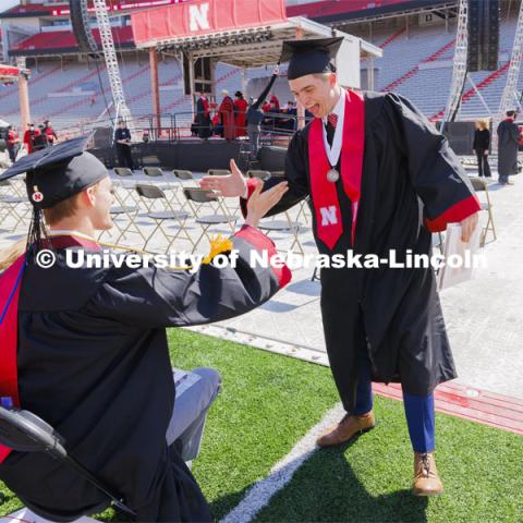 Harrison Wells, standing, and Trenton Sedlacek congratulate each other after Wells received his diploma. Undergraduate Commencement in Memorial Stadium. May 18, 2024. Photo by Craig Chandler / University Communication and Marketing.