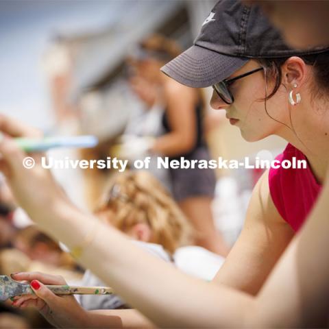 Taryn Hamill, a senior in art, paints on the mural as the group works on the grasses and flowers across the bottom of the mural. ARTS 398 - Special Topics in Studio Art III taught by Sandra Williams. The class painted a mural at the Premier Buick, Chevrolet, and GMC dealership in Beatrice. June 3, 2024. Photo by Craig Chandler / University Communication and Marketing.