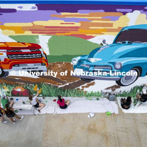 High angle view of students painting a mural. ARTS 398 - Special Topics in Studio Art III taught by Sandra Williams. The class painted a mural at the Premier Buick, Chevrolet, and GMC dealership in Beatrice. June 3, 2024. Photo by Craig Chandler / University Communication and Marketing.