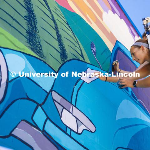 Maddie Vanderbur, wearing a yellow top, a senior in graphic design and Lea Bushey, a senior in graphic design, paint details on the hood ornament of the old pickup in the mural. ARTS 398 - Special Topics in Studio Art III taught by Sandra Williams. The class painted a mural at the Premier Buick, Chevrolet, and GMC dealership in Beatrice. June 6, 2024. Photo by Craig Chandler / University Communication and Marketing.