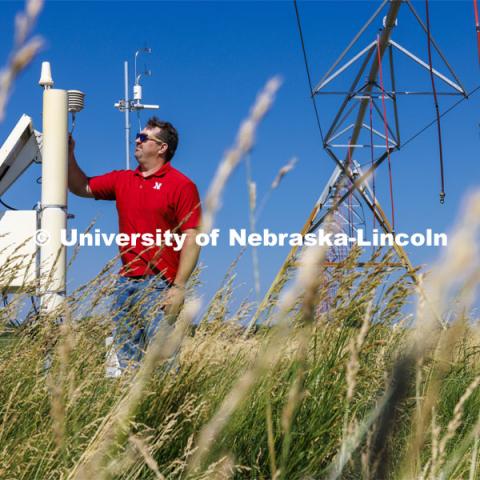 Trenton Franz inspects one of the cosmic ray neutron sensors at the edge of a field at the Eastern Nebraska Research, Extension and Education Center (ENREEC) near Mead, Nebraska. The sensors' readings indicate soil moisture levels. Solar flares, such as those that produced the auroras in Nebraska on May 10-11, trigger electromagnetic interference in the sensors' readings. UNL has taken steps to correct the distortions and ensure data reliability. Franz is using neutron and cosmic ray detectors to see how solar radiation and solar energy such as those that caused Nebraska to view the Northern Lights is effecting precision farming including soil moisture detectors and the GPS in tractors. June 21, 2024. Photo by Craig Chandler / University Communication and Marketing.