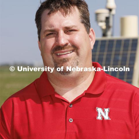 Trenton Franz poses in front of one of the cosmic ray neutron sensors at the edge of a field at the Eastern Nebraska Research, Extension and Education Center (ENREEC) near Mead, Nebraska. The sensors' readings indicate soil moisture levels. Solar flares, such as those that produced the auroras in Nebraska on May 10-11, trigger electromagnetic interference in the sensors' readings. UNL has taken steps to correct the distortions and ensure data reliability. Franz is using neutron and cosmic ray detectors to see how solar radiation and solar energy such as those that caused Nebraska to view the Northern Lights is effecting precision farming including soil moisture detectors and the GPS in tractors. June 21, 2024. Photo by Craig Chandler / University Communication and Marketing.