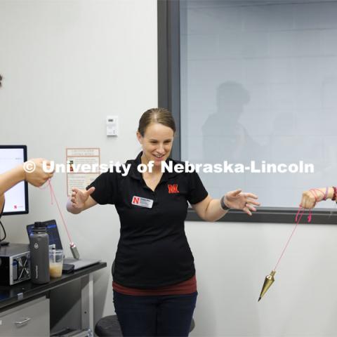 While Chira Khudhur, left, and Bella Thomas swing pendulums, Christine Wittich, Assistant Professor in Civil and Environmental Engineering, explains how various height buildings can sway differently during earthquakes. Sovereign Native Youth STEM Leadership Academy sponsored by MATC. June 24, 2024. Photo by Craig Chandler / University Communication and Marketing.