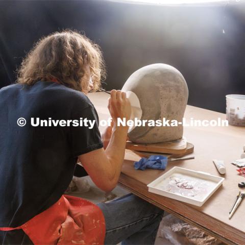 Dawson Adams, a sophomore art student, paints on his sculpture head. Behind the scenes photo for the university's new "Home Again" national advertisement. June 25, 2024. Photo by Kristen Labadie / University Communication.