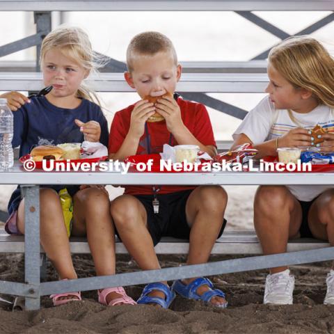 Three young kids eat their lunch on the bleachers at the fair. 4-H Polk County Fair in Osceola, Nebraska. July 19, 2024. Photo by Craig Chandler / University Communication and Marketing.
