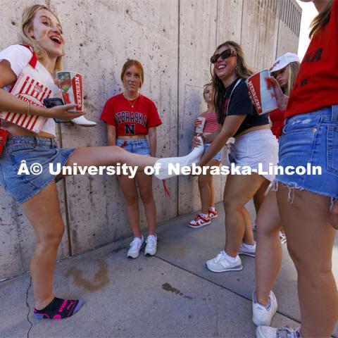 One student helps another remove her boots at the Nebraska football game vs UTEP. August 31, 2024. Photo by Craig Chandler / University Communication and Marketing