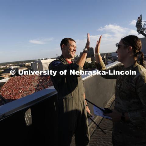 From atop the west stadium roof, Air National Guard Major Bobby Sullivan with the 175th fighter squadron of the 114th fighter wing based out of Sioux Falls, South Dakota, right, high-fives with Air Force ROTC cadet Elena Burgwald as they discuss the radio procedures for the flyover before the game. Nebraska vs. Illinois football game. September 20, 2024. Photo by Craig Chandler / University Communication and Marketing.