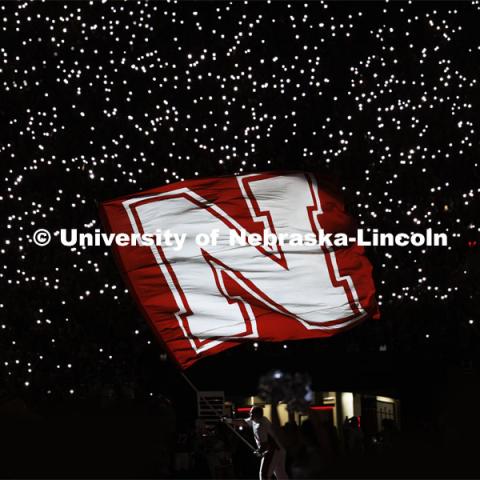 Husker Cheer Squad member Jake Seip waves the Nebraska flag during the end-of-third-quarter light show Friday night with the lights of fan’s phones in the background.  Nebraska vs. Illinois football game. September 20, 2024. Photo by Craig Chandler / University Communication and Marketing.