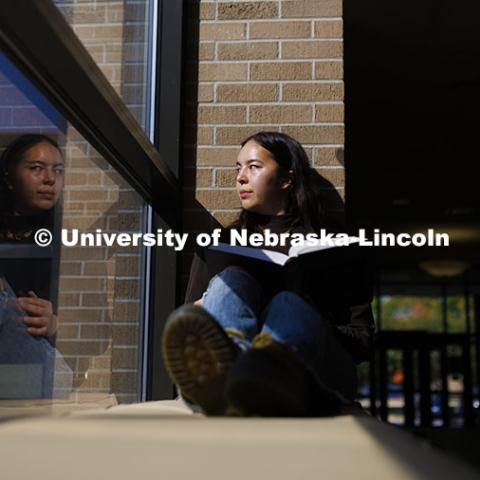 Hana Pham, a first-year law student, appears to be looking at her reflection as she glances outside while studying in the College of Law hallway. College of Law photoshoot. October 10, 2024. Photo by Craig Chandler / University Communication and Marketing.