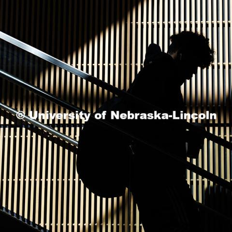 A student is silhouetted as sunlight shines on the wall behind them as they walk downstairs in the College of Business. City Campus. November 12, 2024. Photo by Jordan Opp / University Communication and Marketing.